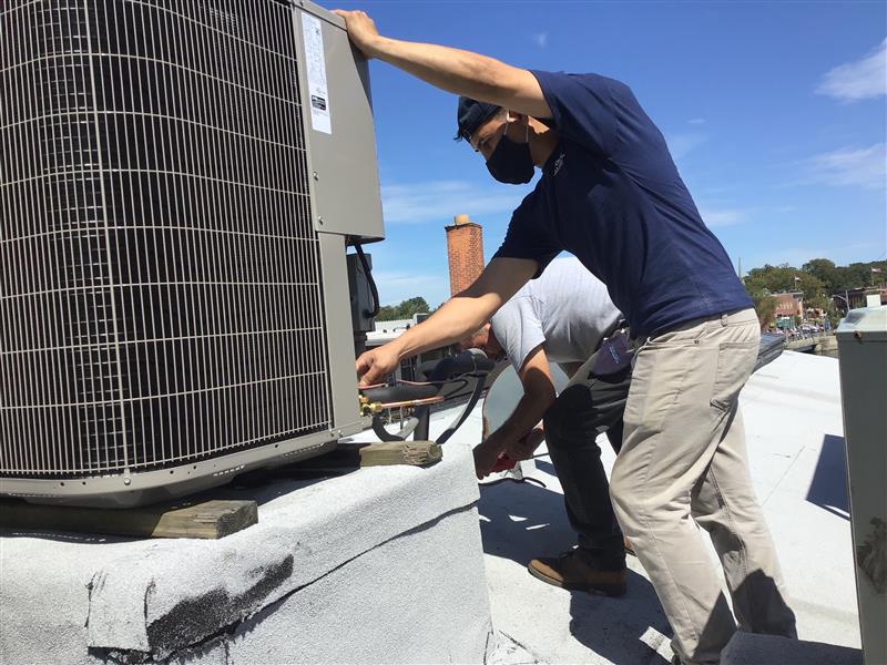 Two men are working on a air conditioner.